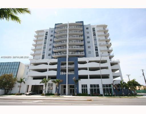 Multi-story concrete high-rise exterior featuring private cantilevered balconies, blue architectural accent panels, and ground-level palm tree landscaping