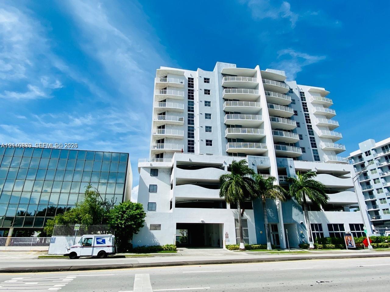 Mid-rise concrete exterior featuring stacked balconies, integrated covered parking levels, and mature palm tree landscaping