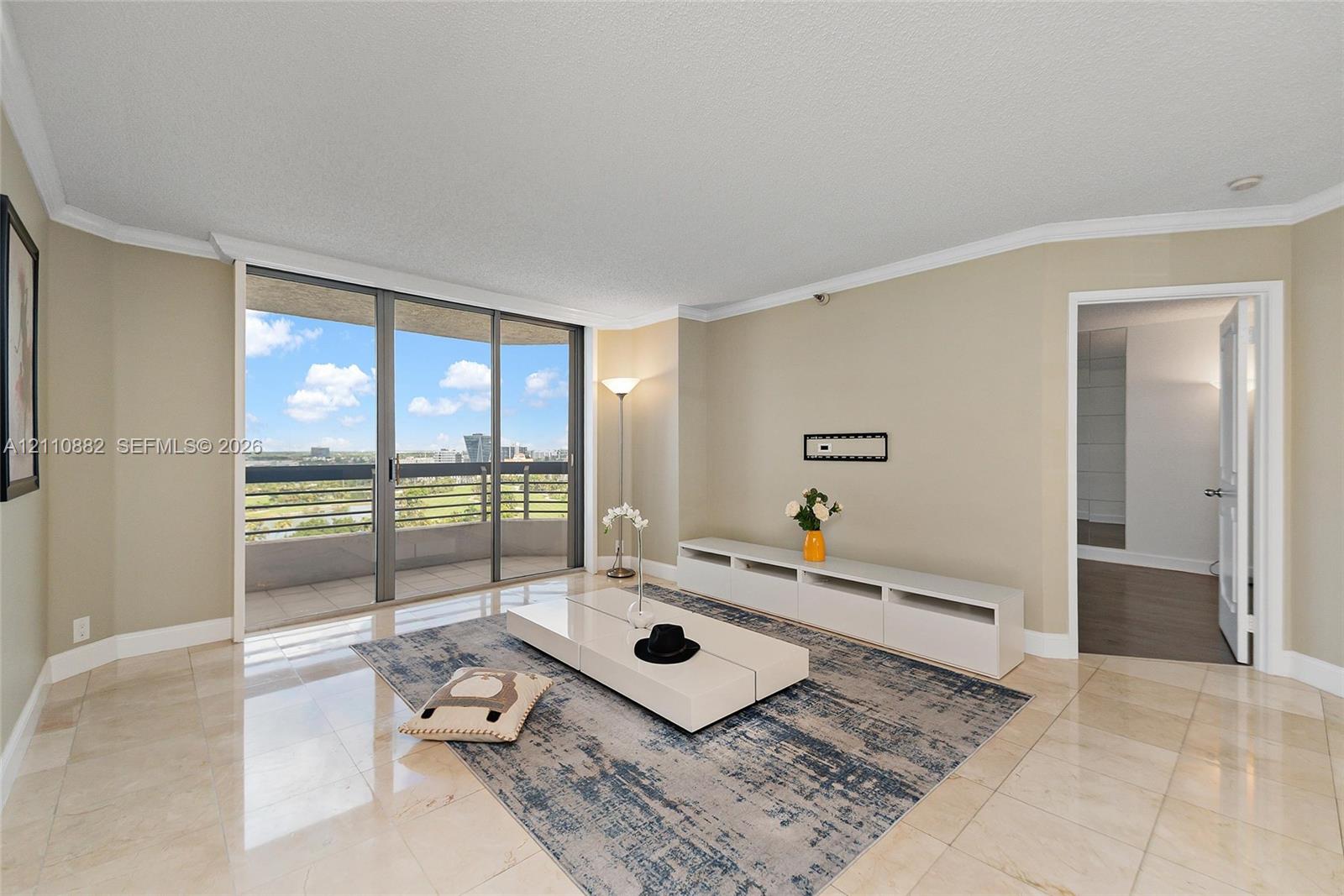 Living area featuring neutral stone flooring, crown molding, and floor-to-ceiling sliding glass doors opening to a private balcony