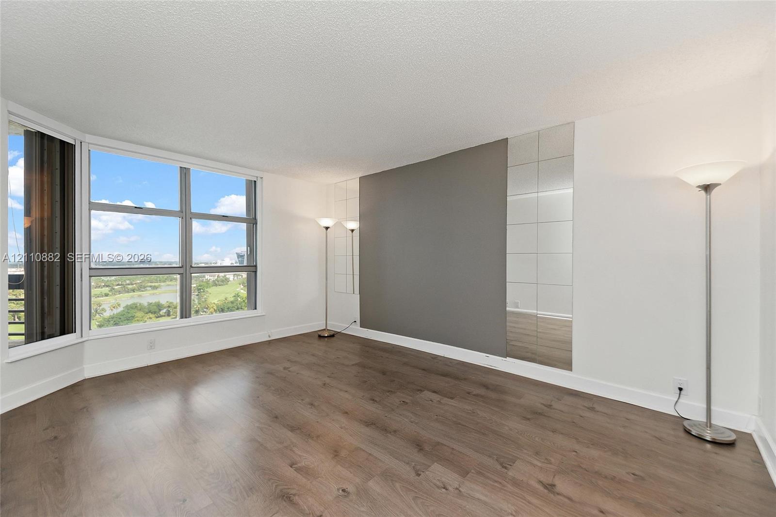 Large floor-to-ceiling bay windows, wood-finish flooring, and a decorative mirrored wall accent Large floor-to-ceiling bay windows, wood-finish flooring, and a decorative mirrored wall accent