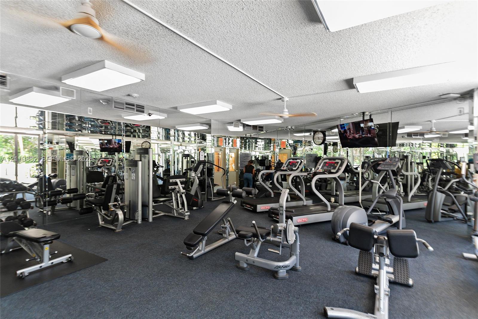 Fitness center featuring mirrored walls, recessed fluorescent lighting, ceiling-mounted paddle fans, and durable flooring