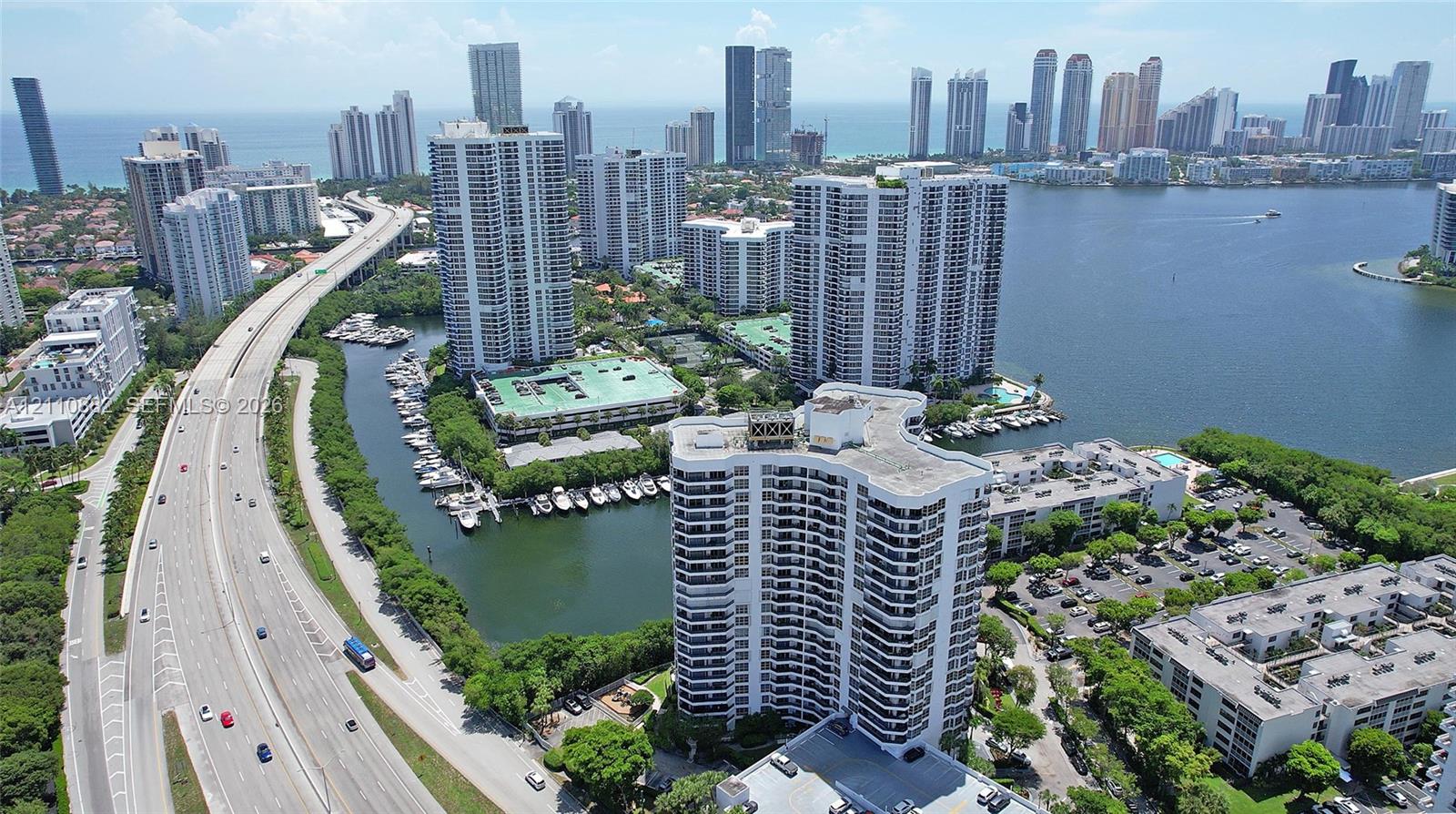 Aerial perspective of high-rise building with balcony tiers, situated along a coastal waterway with surrounding urban infrastructure and tropical landscaping Aerial perspective of high-rise building with balcony tiers, situated along a coastal waterway with surrounding urban infrastructure and tropical landscaping