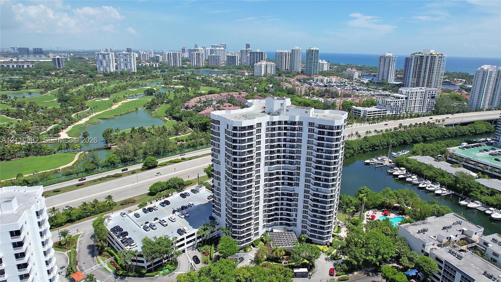 High-rise residential structure featuring a curved architectural profile, multiple levels of balconies, integrated parking garage, and proximity to a waterway marina