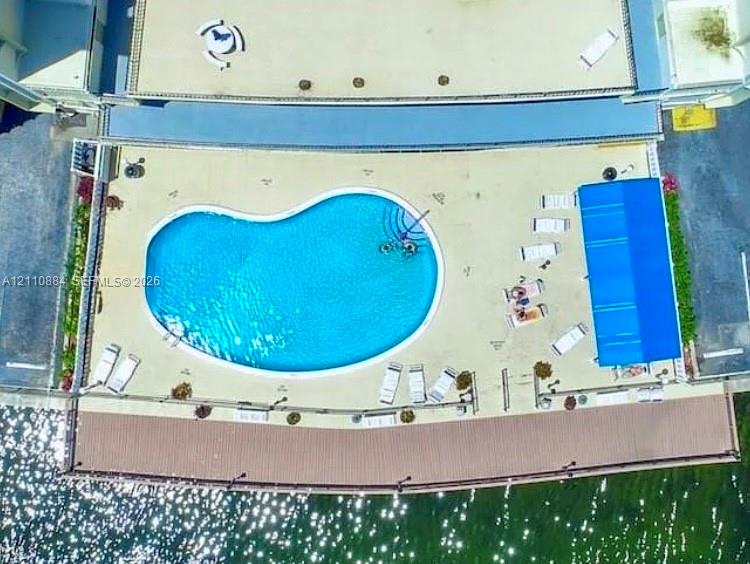 Kidney-shaped pool with integrated stairs, spacious paved deck, blue retractable awning, and waterfront wooden boardwalk