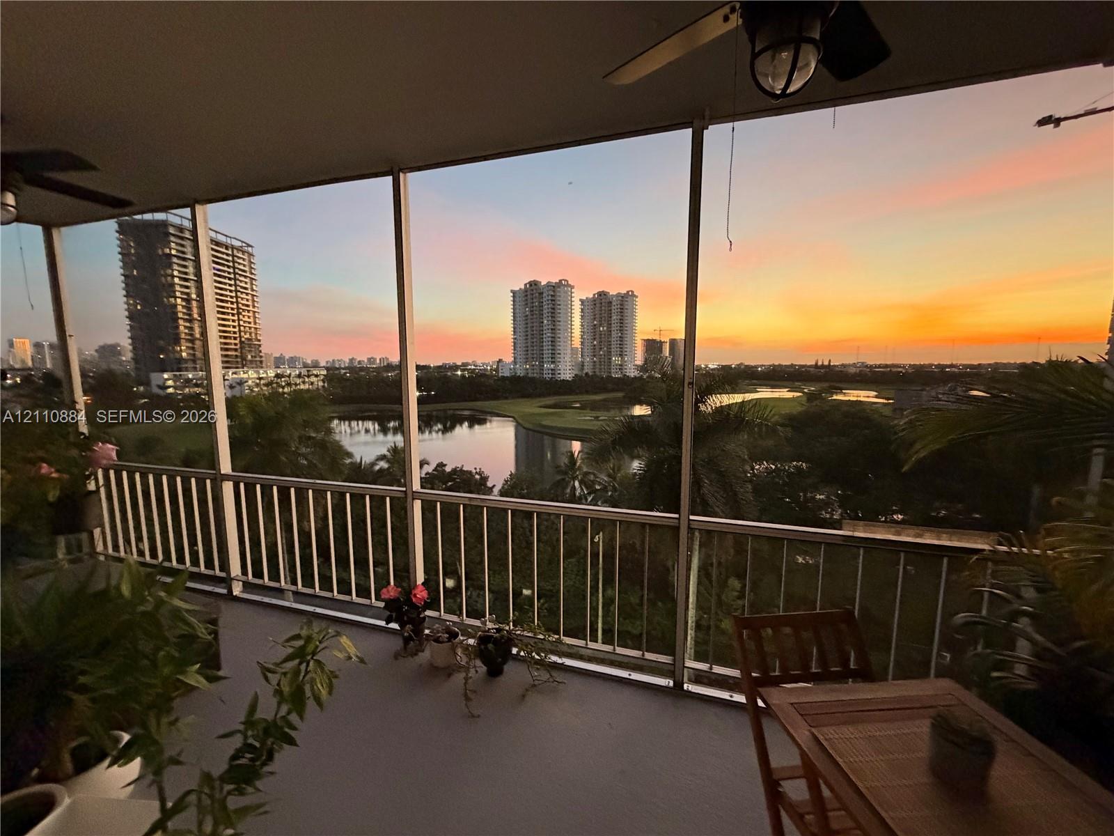 Screened-in balcony featuring a metal railing and ceiling-mounted fans, overlooking a lake and urban skyline