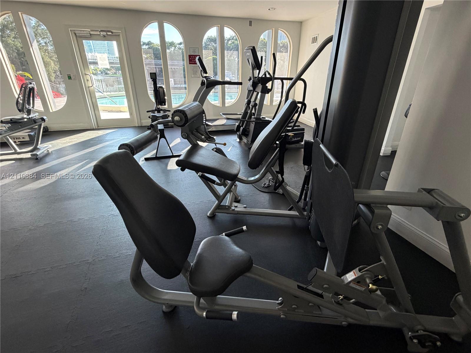Fitness center featuring arched windows, dark rubberized flooring, and glass-paneled entry door