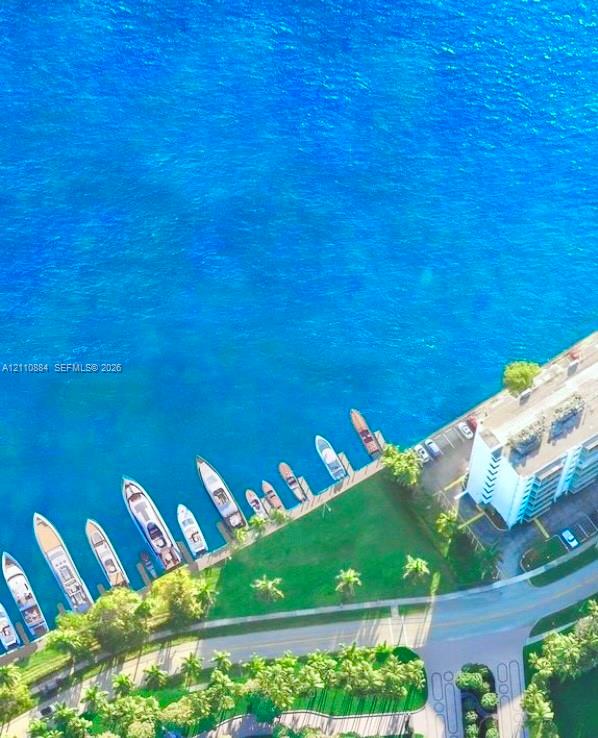 Aerial perspective of waterfront property featuring a concrete pier with deep-water boat slips, manicured grounds, and mature palm trees