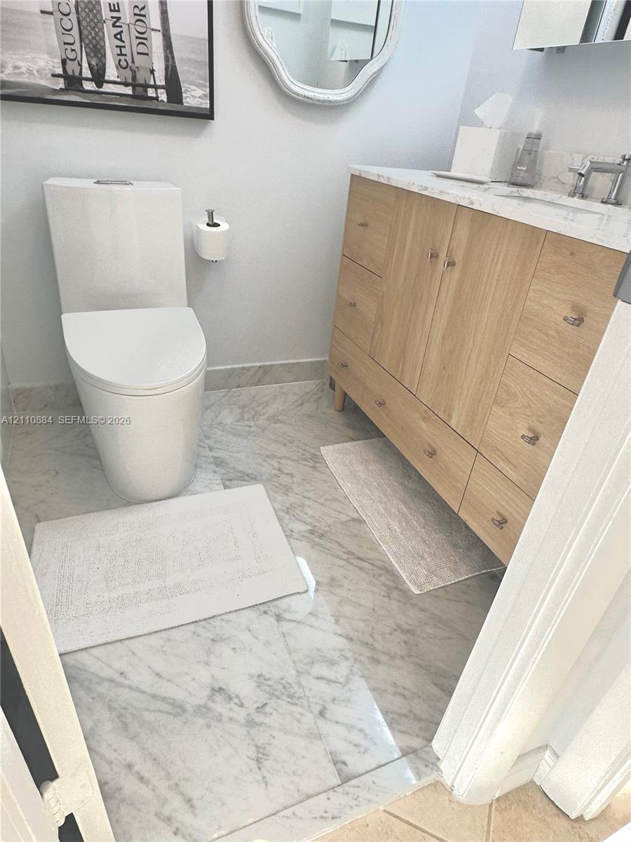 Light-wood cabinetry vanity featuring light-toned stone-finish countertop, integrated sink, and polished metal hardware, paired with premium Calacutta Marble stone-finish tile flooring
