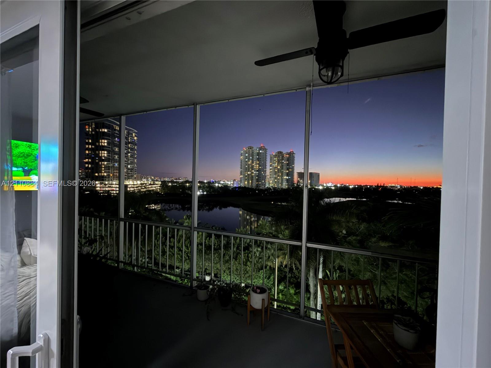 Screened balcony with metal railing, ceiling fan, and skyline and water scenery