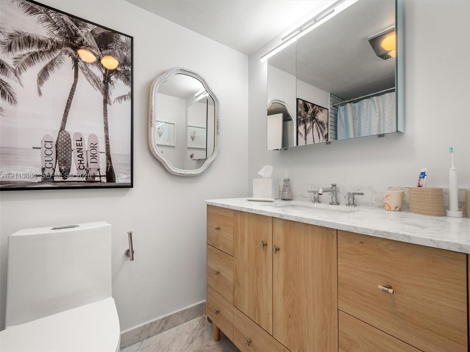 Wood-finish vanity with stone countertop, integrated undermount sink, dual-handle faucet, ultra-modern-mirrored medicine cabinet, and stone-patterned flooring