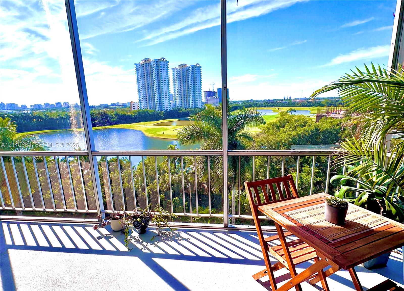 Screen-enclosed balcony featuring a metal railing, overlooking a water feature and manicured landscape