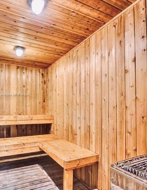Sauna featuring natural wood-paneled walls and ceiling, built-in tiered wooden benches, slatted wooden floor decking, and stainless steel heater unit with wall-mounted lighting