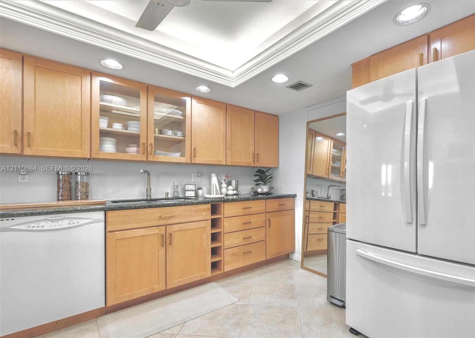 Kitchen featuring custom, sollid wood cabinetry, integrated glass-front display cabinets, jade stone countertops, recessed lighting, and a tray ceiling