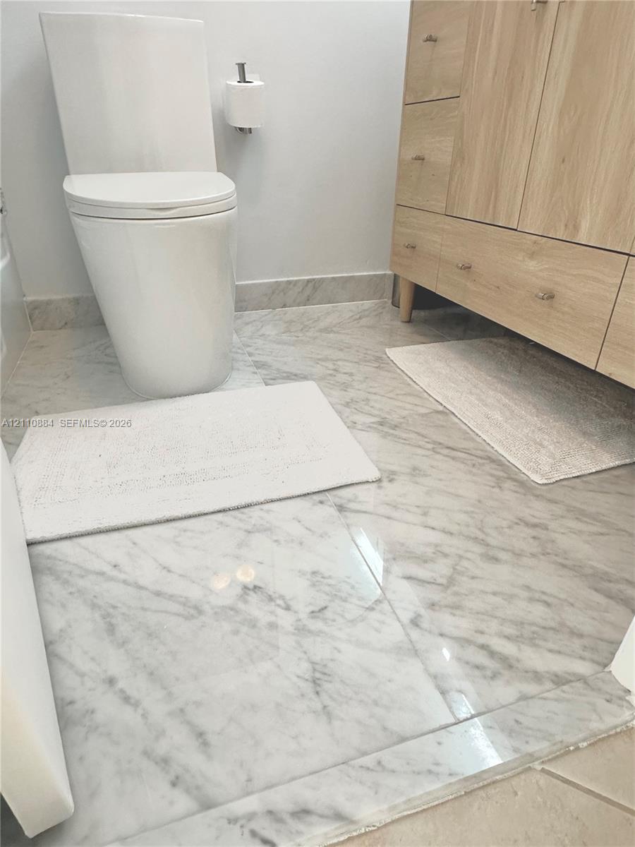 Bathroom featuring a wood-finish vanity with drawer cabinetry, stone-tiled flooring, and a new, ultra-modern one-piece toilet on luxe Calacutta Marble