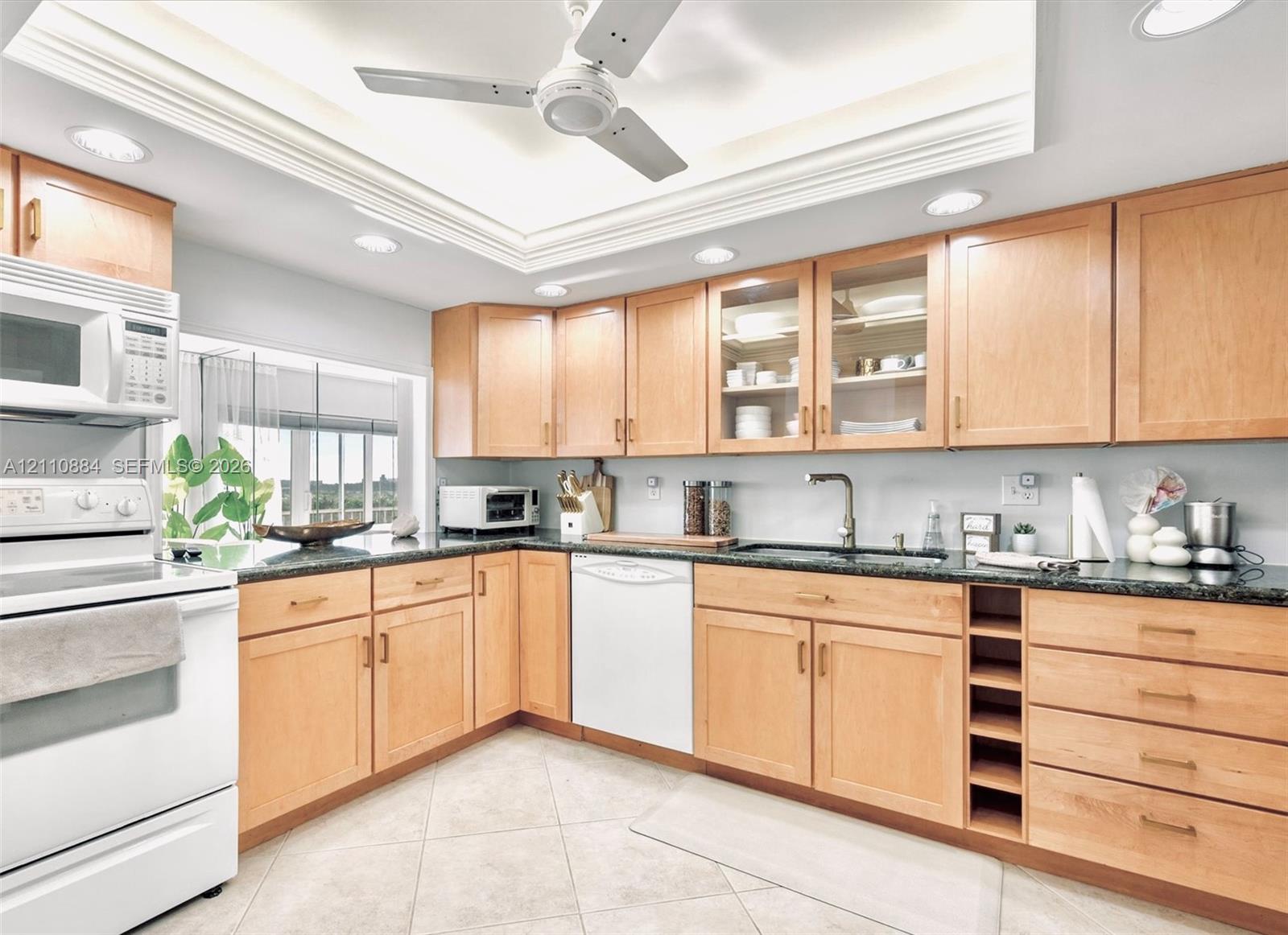 Kitchen featuring custom, solid maple wood cabinetry with glass-front uppers, jade stone countertops, built-in wine storage, recessed lighting, and a tray ceiling with a central ceiling fan