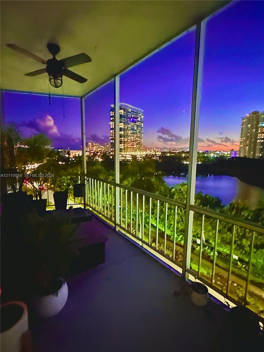 Screened-in balcony featuring a ceiling-mounted fan and metal railing, overlooking water and urban skyline