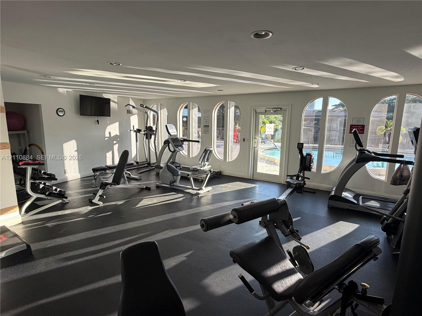 Fitness center featuring rubber flooring, recessed lighting, and arched windows with exterior pool access
