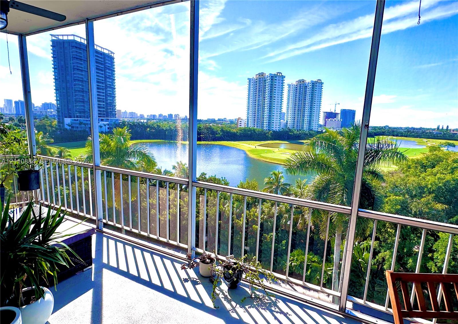 Screened balcony featuring metal railings, overhead ceiling fan, and concrete flooring, overlooking a lake, golf course, and tropical oasis landscape Screened balcony featuring metal railings, overhead ceiling fan, and concrete flooring, overlooking a lake, golf course, and tropical oasis landscape