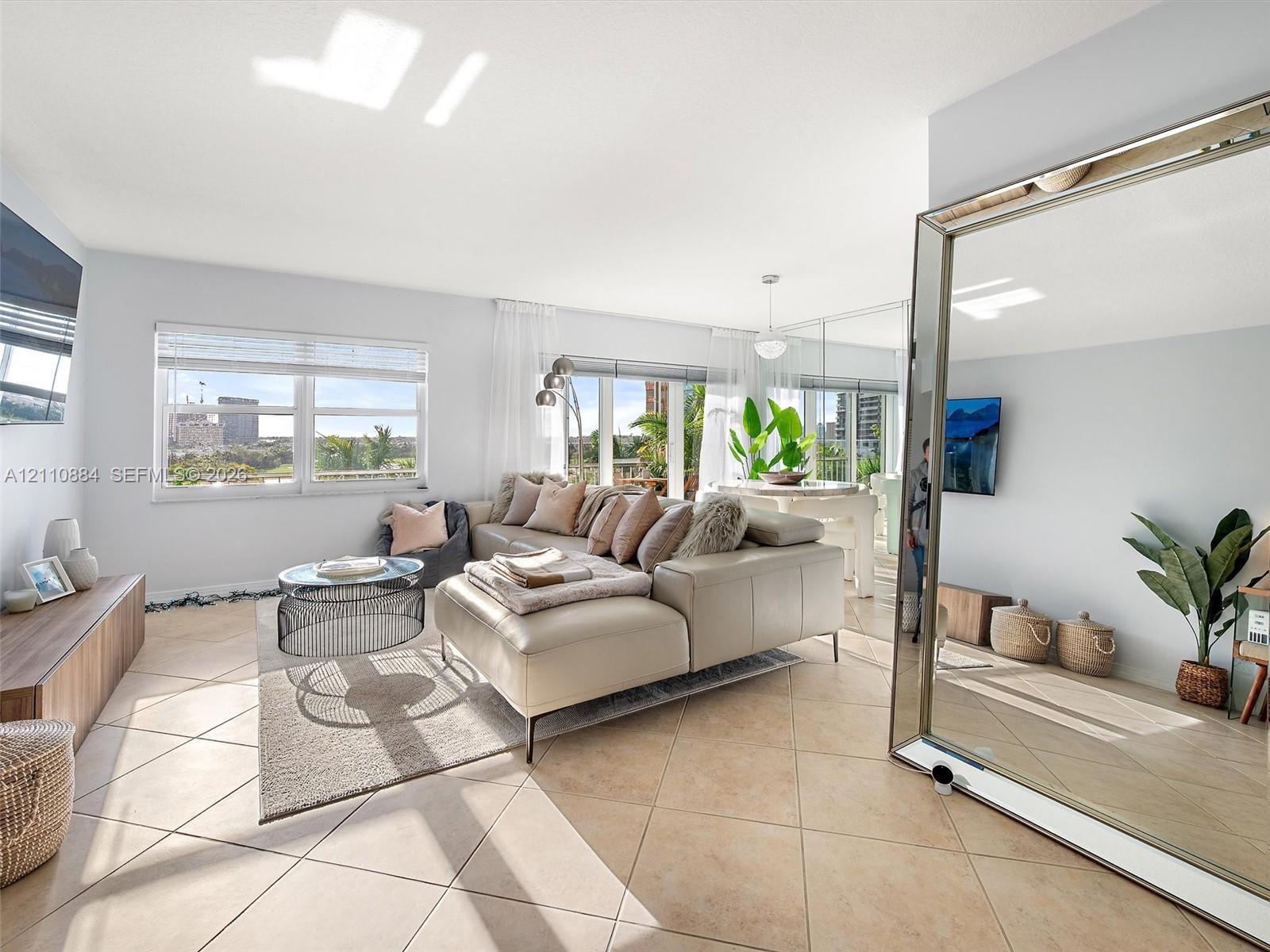 Open-concept living space featuring large-format ceramic tile flooring, expansive windows with exterior cityscape, and wall-to-wall mirror paneling Open-concept living space featuring large-format ceramic tile flooring, expansive windows with exterior cityscape, and wall-to-wall mirror paneling