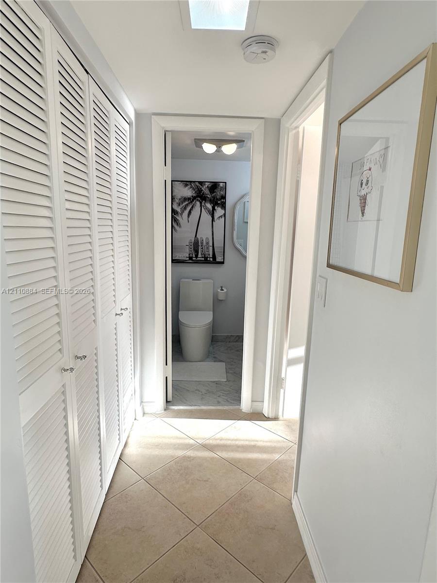 Hallway featuring floor-to-ceiling white louvered closet doors, neutral tile flooring and a newly renovated XXL closet space