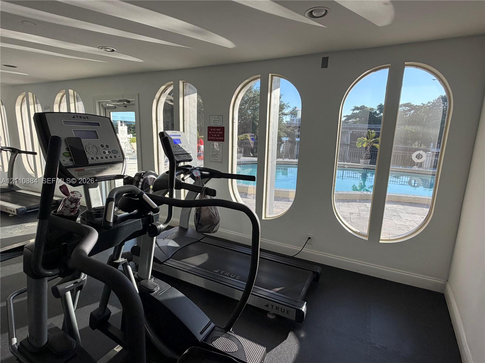 Fitness area featuring arched windows, recessed lighting, and rubber flooring, with direct exposure to a swimming pool