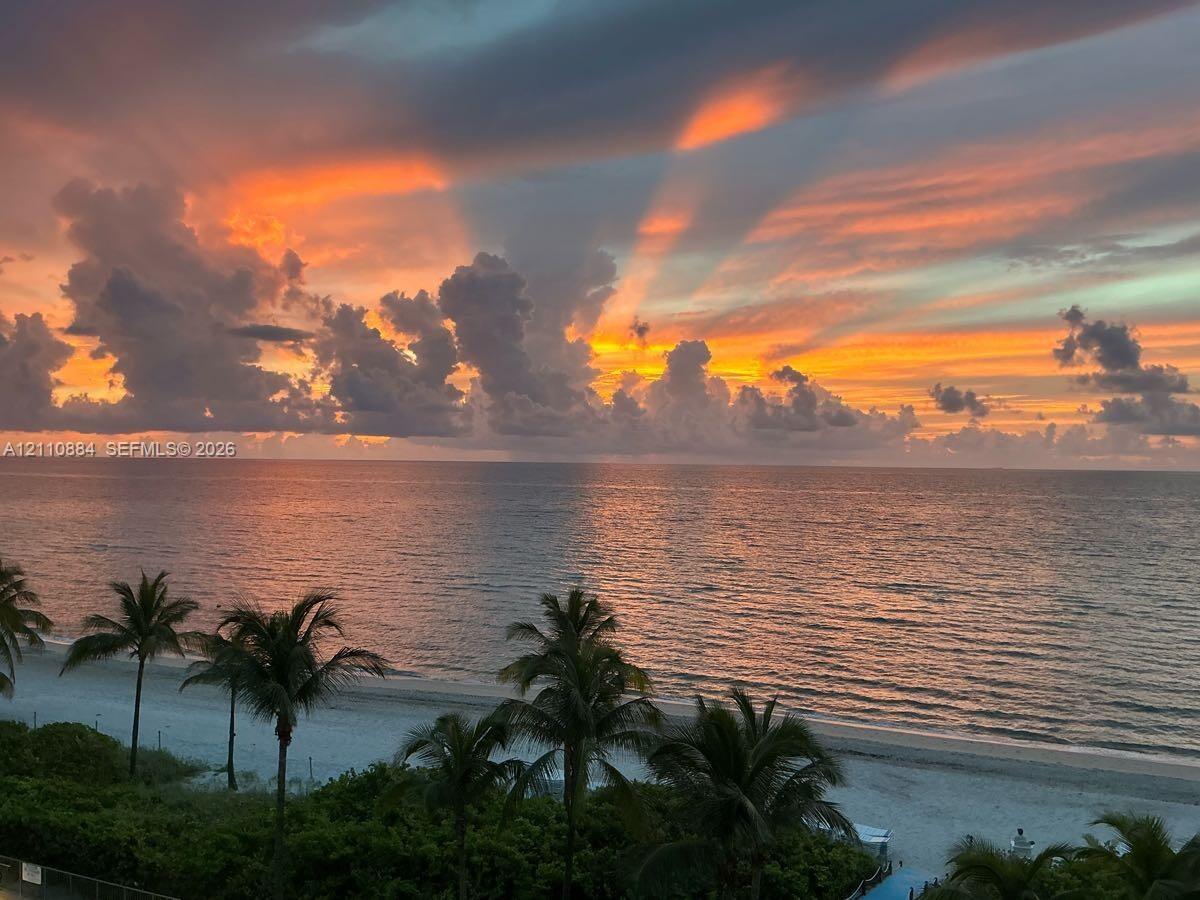 Direct waterfront access featuring a sandy beach, tropical palm trees, and panoramic ocean scenery at sunset