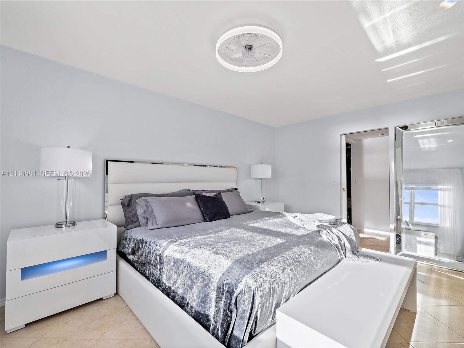 Neutral-toned interior space featuring light-colored tile flooring, smooth walls, and a recessed, circular dimmable LED ceiling light / fan fixture with remote