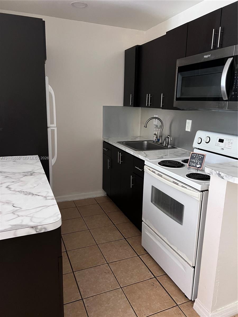 Kitchen featuring dark cabinetry, stone-finish laminate countertops, ceramic tile flooring, and integrated stainless steel appliances