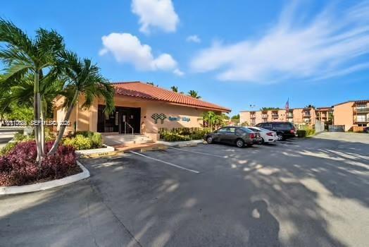Commercial structure featuring a terracotta tile roof, stucco exterior, paved parking area, and palm tree landscaping