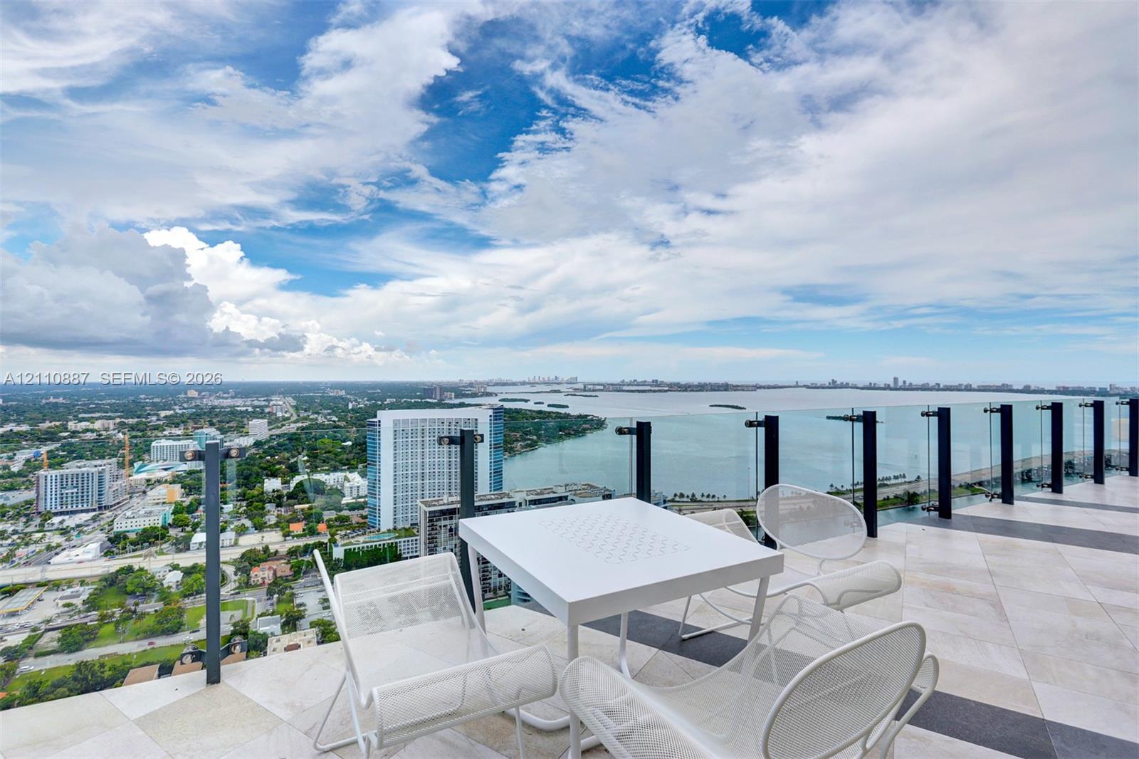 Expansive high-rise terrace featuring light-toned stone tile flooring and a frameless glass balcony railing