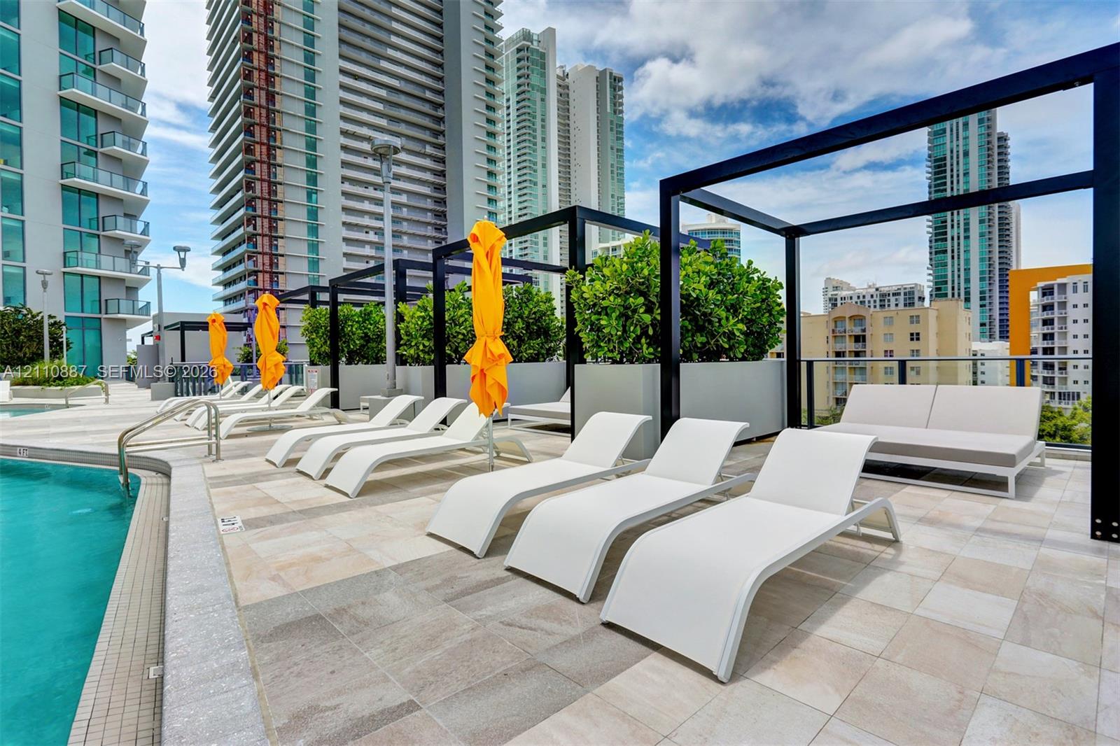 Swimming pool deck featuring stone-tiled flooring, black metal pergola structures, and integrated planter boxes with shrubbery
