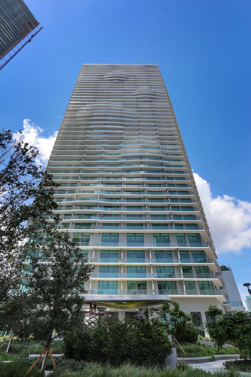 High-rise residential tower featuring a glass facade, undulating exterior balconies, floor-to-ceiling windows, and contemporary architectural design