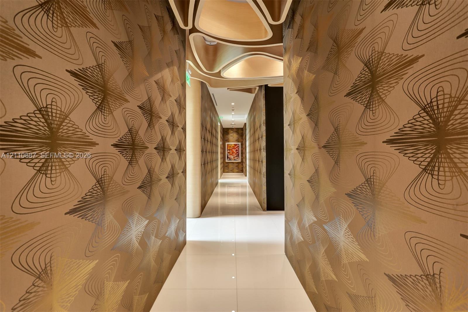 Hallway featuring patterned metallic wall coverings, polished light-toned tile flooring, and custom sculptural geometric ceiling detailing
