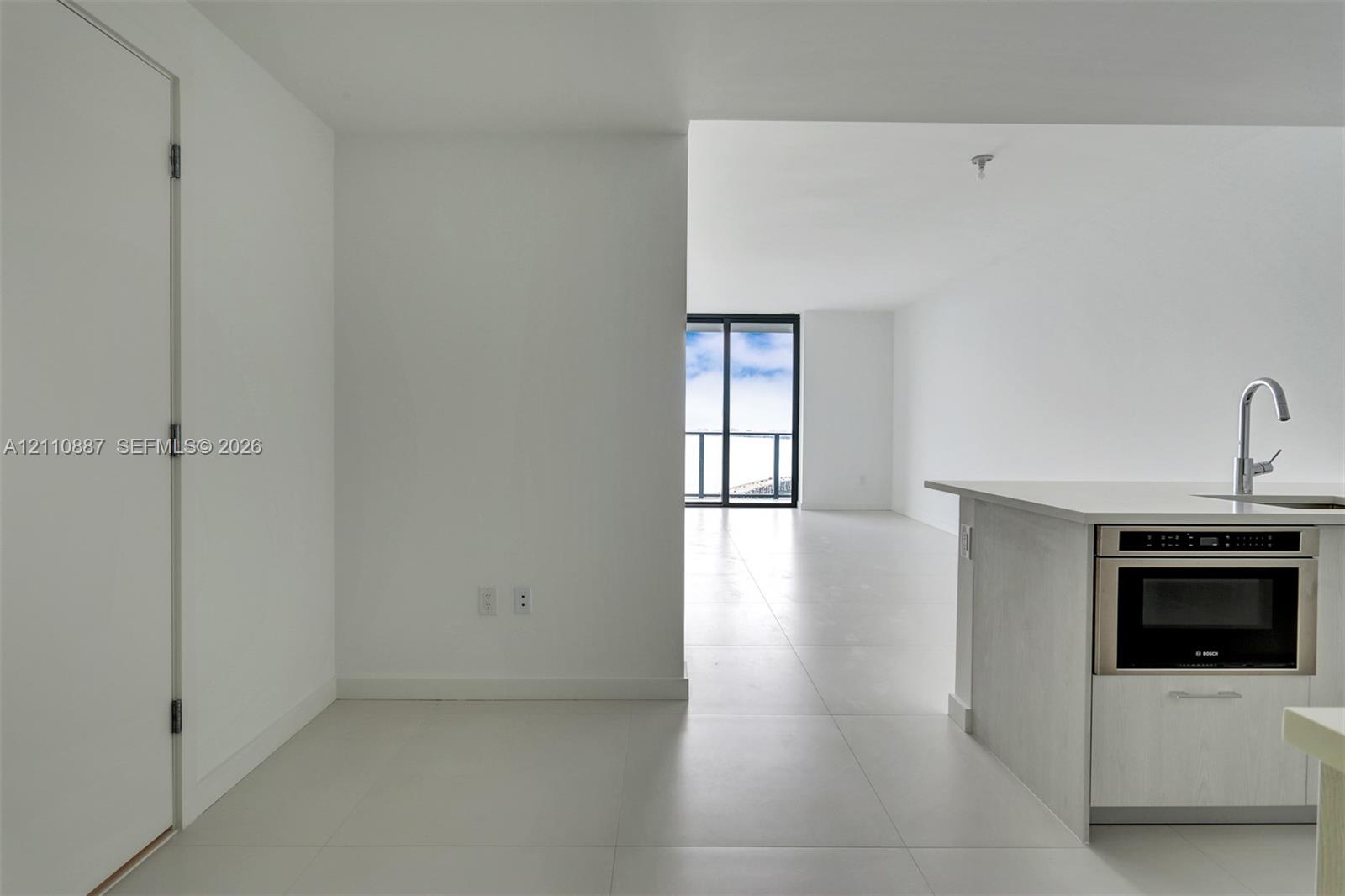 Kitchen area featuring light-finish cabinetry, quartz-style countertops, an integrated stainless steel microwave, and a stainless steel arched faucet, complemented by large-format tile flooring and floor-to-ceiling glass sliding doors