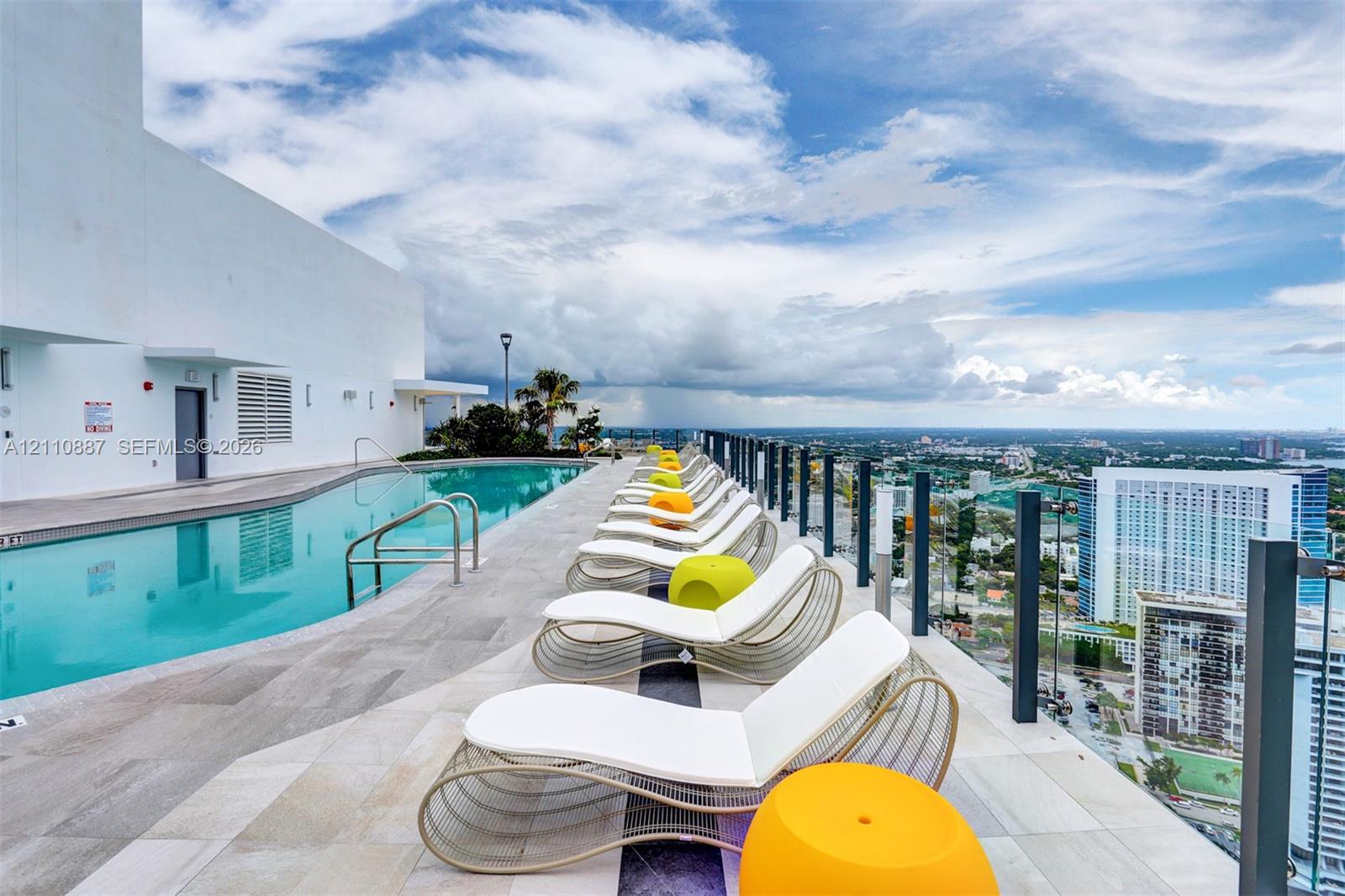 Rooftop swimming pool featuring stone-tile decking, metal safety railings, and expansive urban scenery