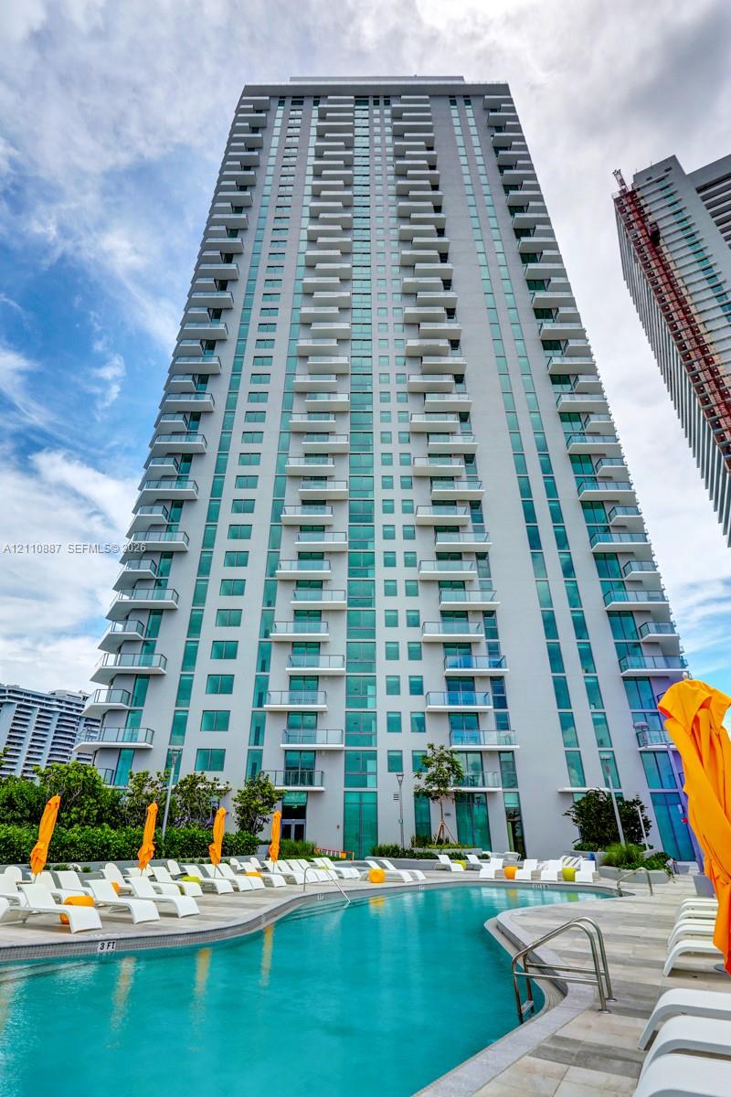High-rise residential tower featuring tiered glass-railed balconies, exterior masonry facade, and an outdoor swimming pool with stone-tiled decking