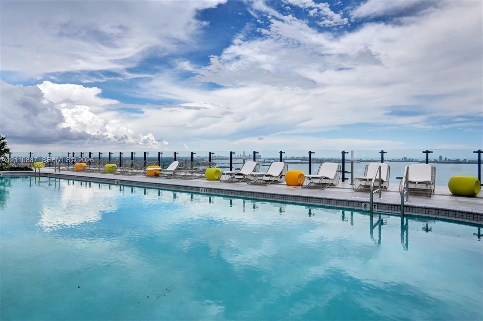 Infinity-edge pool featuring a glass-panel railing, tiled perimeter, and water-level entry steps