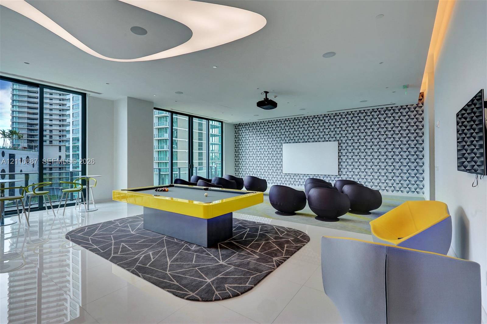 Contemporary media room featuring a sculptural ceiling fixture, patterned accent wall, floor-to-ceiling windows, and glossy stone-finish flooring