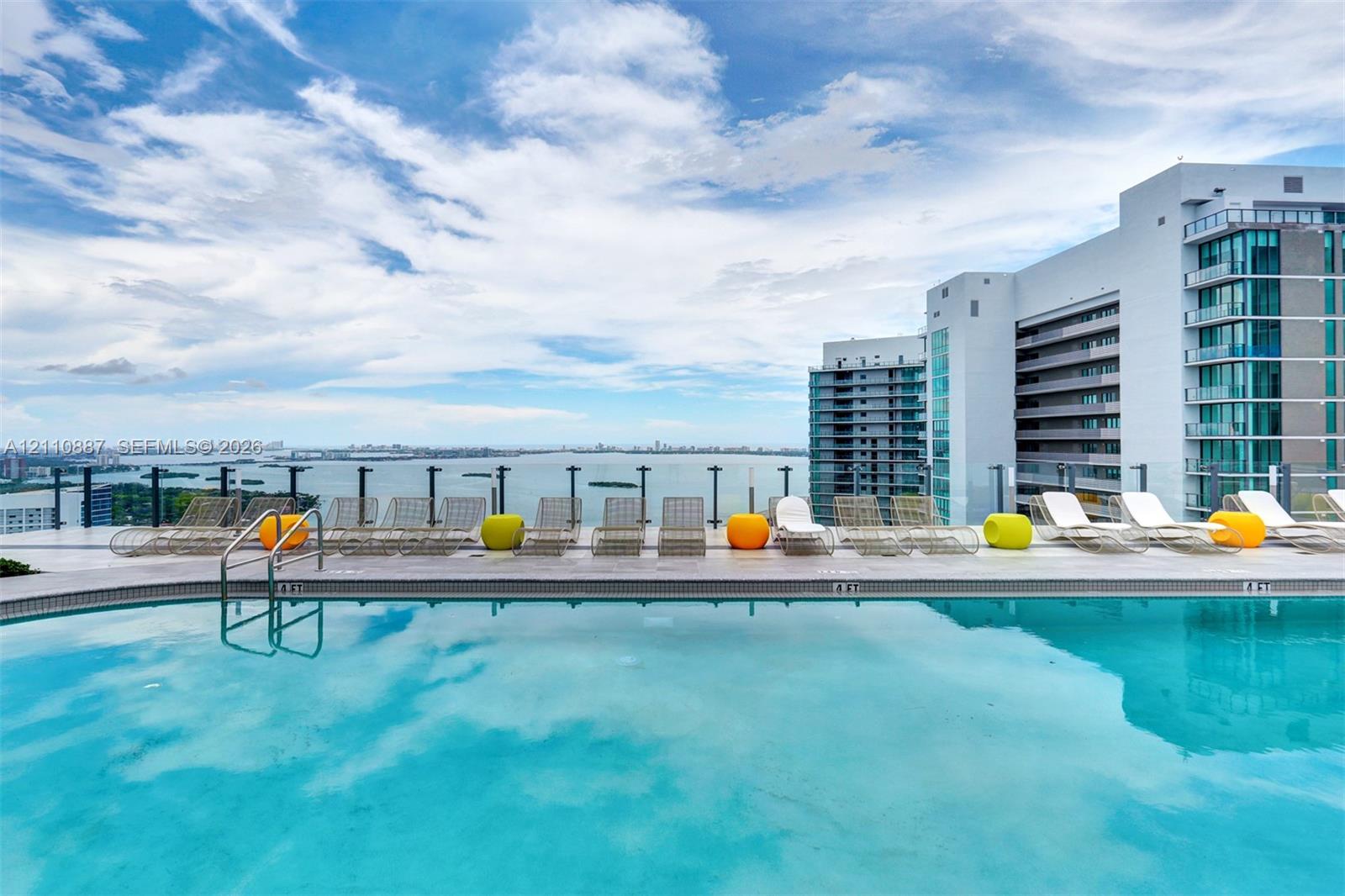 Rooftop swimming pool featuring a tiled deck, glass panel railings, and horizon water scenery