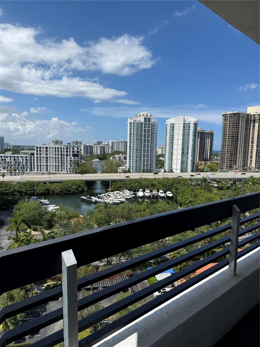 Balcony featuring horizontal black metal railing overlooking a waterway, marina with docked boats, and urban cityscape
