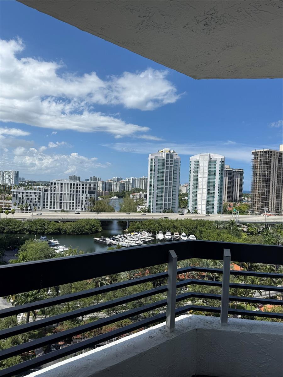 Private balcony featuring a black metal railing overlooking a waterway, boat slips, and an urban cityscape