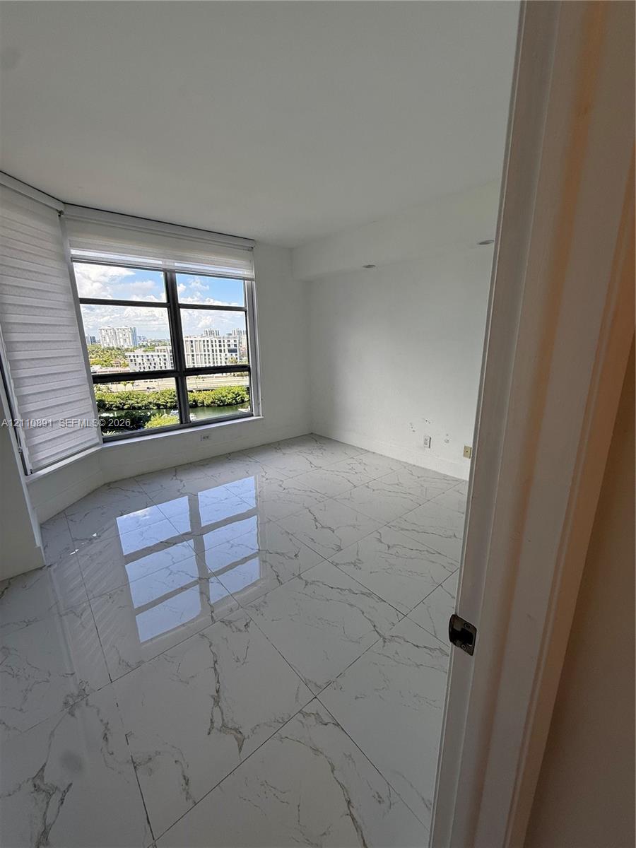 Room featuring large-format veined tile flooring and floor-to-ceiling windows with roller shades