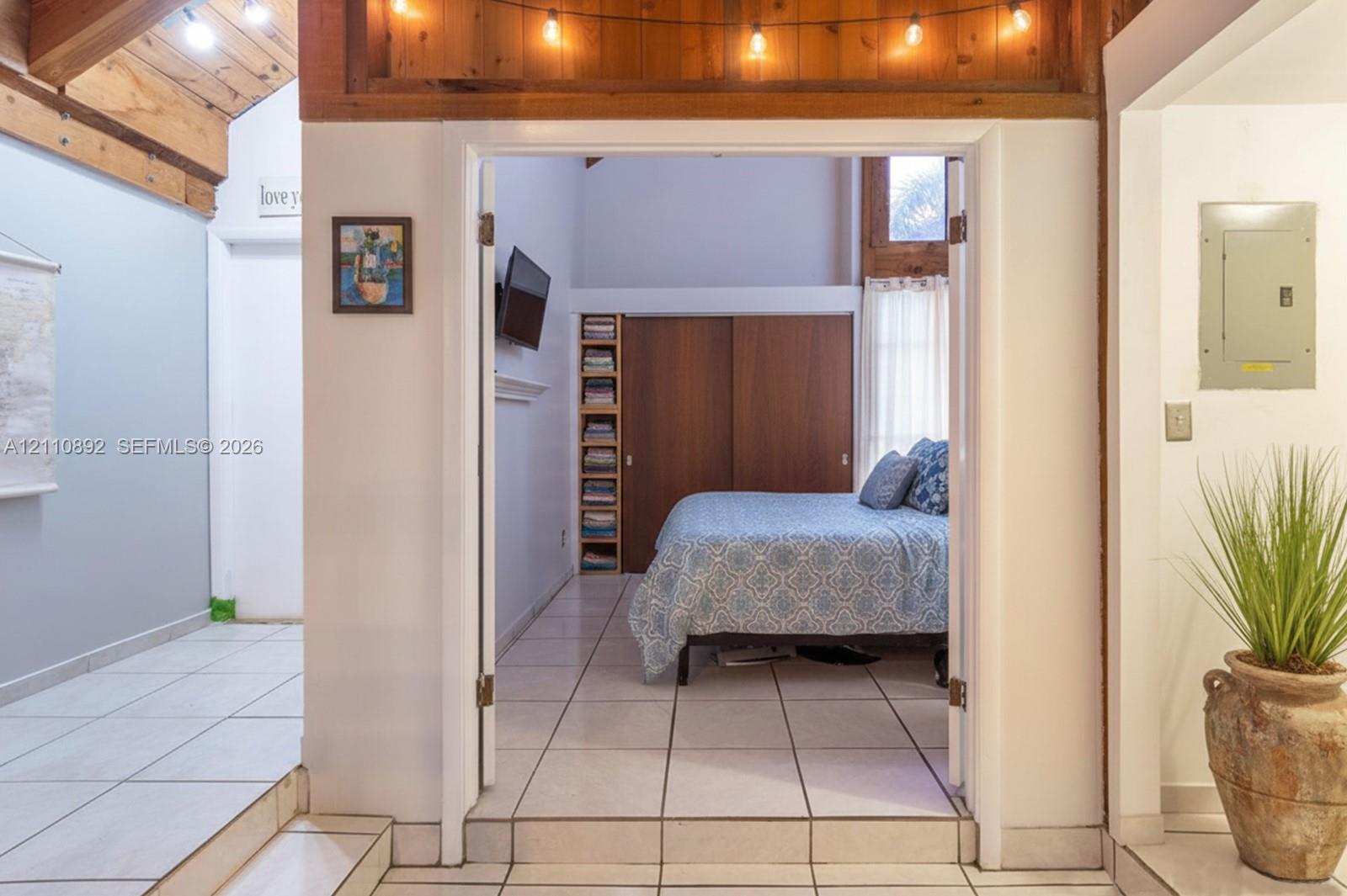 Vaulted ceiling with exposed wood beams, tile flooring, built-in shelving, and dual-panel wood sliding closet doors
