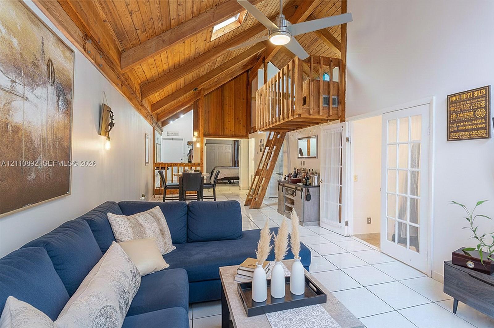 Vaulted timber-plank ceiling featuring exposed beams, skylight, wooden loft structure with integrated ladder, tile flooring, and French doors with glass panes Vaulted timber-plank ceiling featuring exposed beams, skylight, wooden loft structure with integrated ladder, tile flooring, and French doors with glass panes