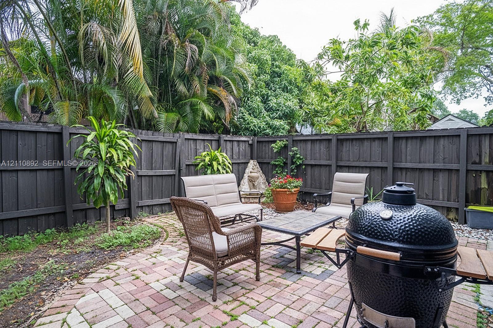 Private courtyard featuring a patterned brick paver patio, dark wood-finish perimeter fencing, and established tropical landscaping