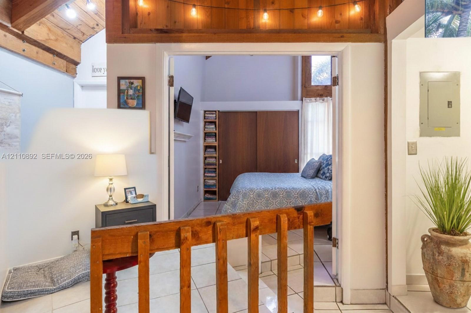 Exposed wood ceiling beams, white ceramic tile flooring, floor-to-ceiling wooden built-in shelving, sliding wood closet doors, and wood-railing partition Exposed wood ceiling beams, white ceramic tile flooring, floor-to-ceiling wooden built-in shelving, sliding wood closet doors, and wood-railing partition
