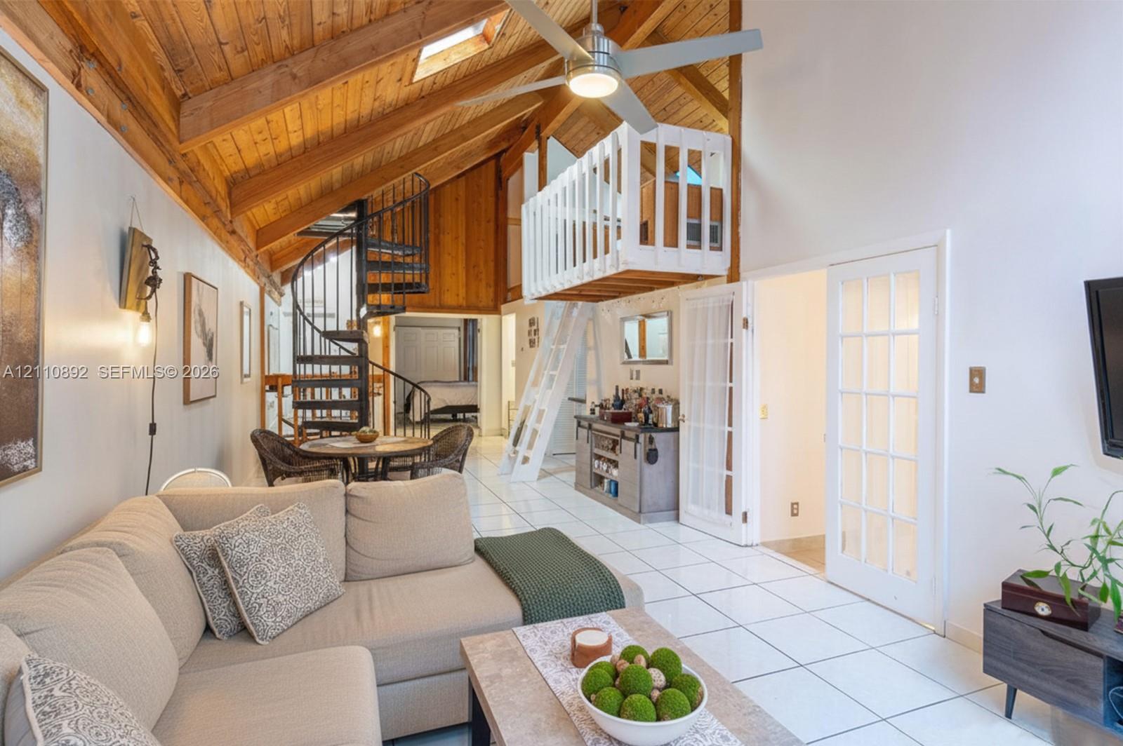 Vaulted wood-paneled ceiling with skylight, exposed wooden beams, metal spiral staircase, white-railed loft level, and French doors with glass panes Vaulted wood-paneled ceiling with skylight, exposed wooden beams, metal spiral staircase, white-railed loft level, and French doors with glass panes
