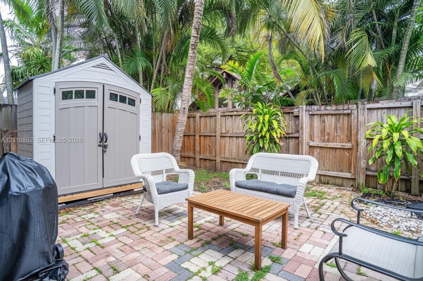 Exterior storage shed with double-door entry, multi-toned paver patio, wood-style privacy fencing, and mature palms