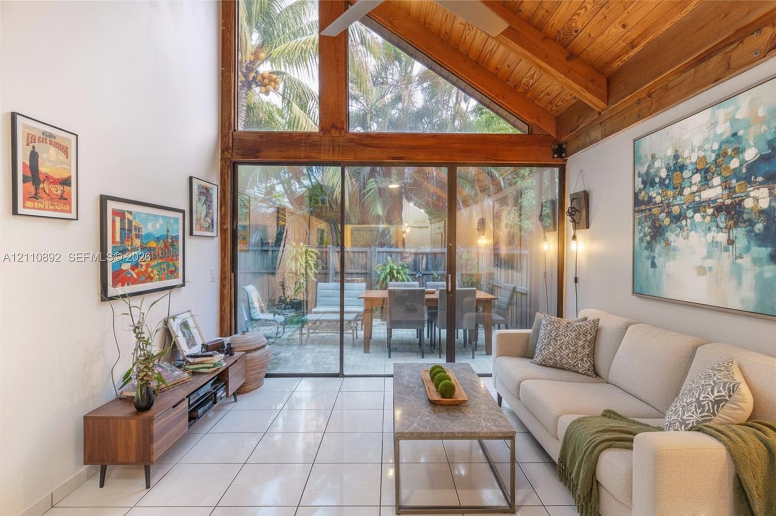 Vaulted ceiling with exposed wood beams, full-height windows, floor-to-ceiling glass sliding doors, and light-toned tile flooring Vaulted ceiling with exposed wood beams, full-height windows, floor-to-ceiling glass sliding doors, and light-toned tile flooring