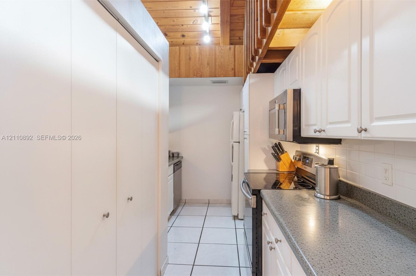 Kitchen featuring white cabinetry, solid-surface countertops, a tiled backsplash, wood-plank ceiling, and floor tiles